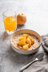 Oatmeal with peaches and nuts  in a bowl on a light background with honey