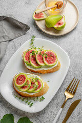 Sweet toasts with fresh figs, cheese, thyme, and honey on a gray background.