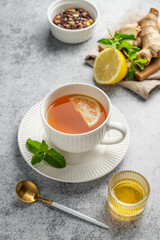 Tea with lemon, ginger, honey, and mint in a cup on a gray background with citrus fruits and herbs.