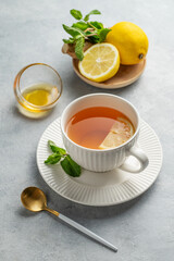 Hot tea with lemon, ginger, honey, and mint in a cup on a light background with citrus fruits
