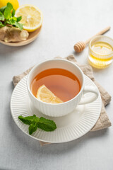 Hot tea with lemon, ginger, honey, and mint in a cup on a light background with citrus fruits