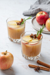 Two glasses of apple cider with cinnamon, anise, and rosemary on a marble background with fresh fruits