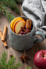 A cup of red mulled wine with spices, orange, apple slices and cranberry on a wooden background