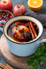 A pot of red mulled wine with spices, orange, apple slices, and cranberries on a wooden board