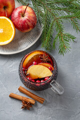 A cup of red mulled wine with spices, orange, apple slices and cranberry on a blue background