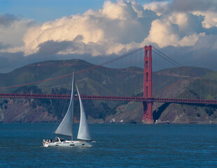 A beautiful modern sailboat sails on a windy day in San Francisco bay in front of the Golden Gate Bridge and the Marin Headlands .