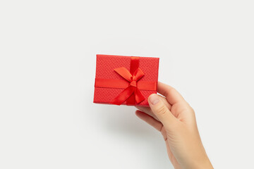 Hand holding a small red gift box with a ribbon