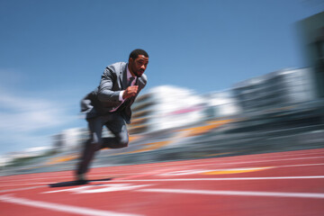 Businessman in a suit sprinting on a running track from the starting line with motion blur and city background