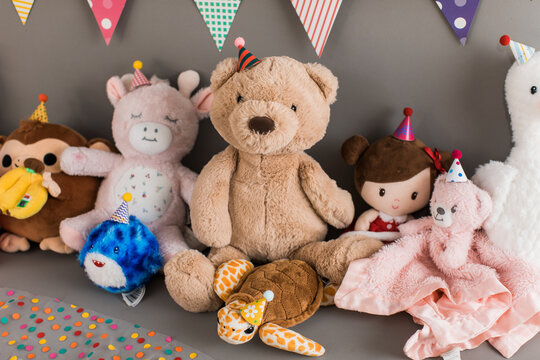 Closeup un Stuffed animals and plush toys with birthday hats sitting under a banner on gray background ready to celebrate a birthday