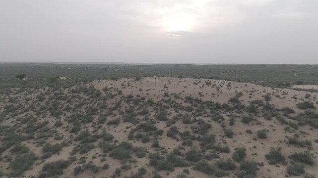 Aerial view of Khuri Sand Dunes in Thar Desert, Jaisalmer during monsoon sunset, showing golden dunes, desert vegetation like Khejri & Babool trees, and warm light reflecting on sand under cloudy sky