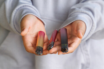A person's hands holding three colorful, sleek disposable electronic cigarettes or vape pods.