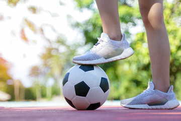 A person in white running shoes steps on a classic black and white soccer ball on a sports court.