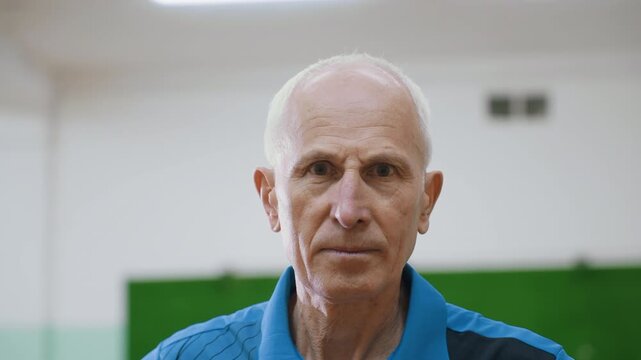 Close up of elder man with hand on waist lifting head slowly in thoughtful pose indoors, showing wisdom, reflection, maturity, and calm expression in sports hall background