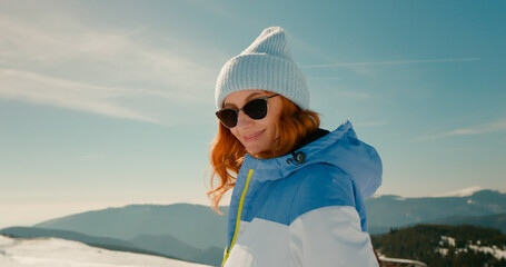 Winter lover woman turns to the camera and smiles in the snowy mountains during vacation. Adventurous tourist facing the beauty of the snowy mountain peaks. Travelling and exploring concept.