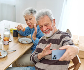 Portrait of a senior mature couple having a healthy breakfast and taking making a selfie with a smart phone mobile phone in the morning at home