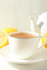 Aromatic tea in cup, lemons and teapot on white table, closeup