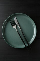 Clean ceramic plate and cutlery on black wooden table, top view