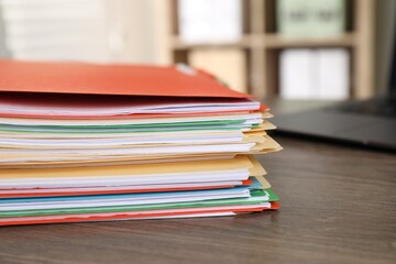Many folders with documents and laptop on wooden desk, closeup