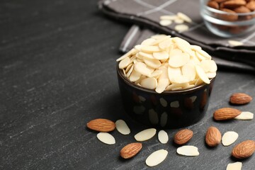 Fresh almond flakes in bowl and whole nuts on grey table, closeup. Space for text
