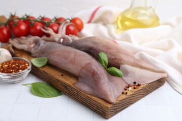 Fresh raw squids, tomatoes and spices on white tiled table, closeup
