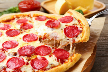 Taking piece of delicious pepperoni pizza at wooden table, closeup
