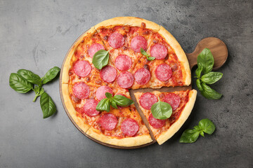 Delicious cut pepperoni pizza with fresh basil on grey table, top view