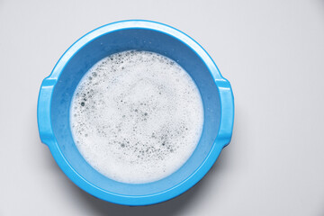 Blue plastic basin with water and foam on grey background, top view