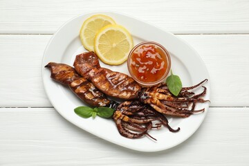 Tasty cooked squids served with lemon, sauce and basil on white wooden table, top view