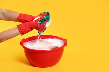 Woman washing clothes in plastic basin on yellow background, closeup. Space for text