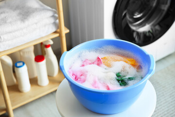 Plastic basin with laundry and soapy water on white table in bathroom, closeup