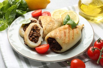 Pieces of tasty grilled squid stuffed with mushrooms, basil, tomatoes and lemon on grey table, closeup
