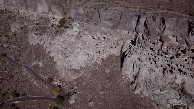 Drone flying over the ancient cave city of Vardzia in Georgia &mdash; a vast monastery and fortress carved into a mountain cliff, illuminated by summer sunlight with birds flying nearby