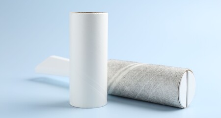 Lint roller with used sticky tape and new adhesive roll on light blue background, closeup