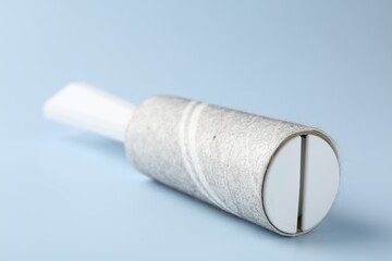 Lint roller with used sticky tape on light blue background, closeup