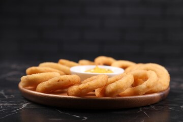 Fried squid rings with sauce on black marble table, closeup. Space for text