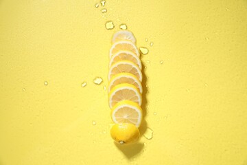 Fresh lemon slices on glass surface with water drops on yellow background, top view