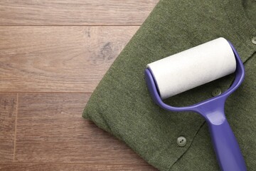Sticky lint roller and shirt on wooden table, top view. Space for text