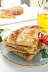 Pieces of delicious Megrelian khachapuri with parsley and tomatoes on white wooden table, closeup
