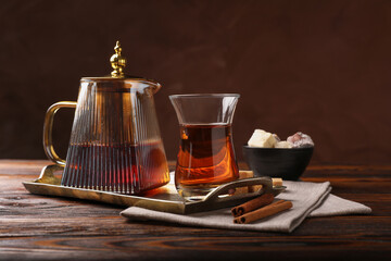 Tasty Turkish tea in glass cup, brown sugar, cinnamon, sweets and teapot on wooden table against color background