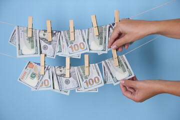 Money laundering. Woman hanging banknote on clothesline against light blue background, closeup
