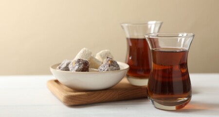 Traditional Turkish tea in glasses and sweets on white wooden table, closeup