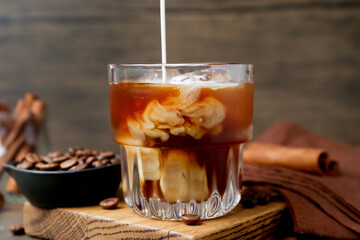 Pouring milk into iced coffee at wooden table, closeup