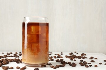 Tasty iced coffee with milk and beans on white wooden table. Space for text