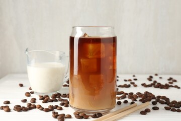 Tasty iced coffee with milk and beans on white wooden table