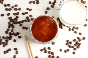Tasty iced coffee, milk and beans on white wooden table, flat lay