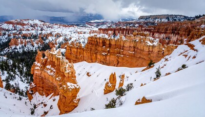 Winter landscape showcasing snow-covered orange and red rock formations, showcasing hoodoos and canyons under a cloudy sky