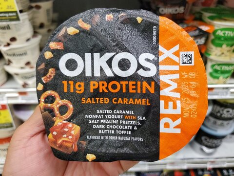 Delaware, U.S.A - Oct 15, 2025 - Close-up of an Oikos Remix Salted Caramel nonfat Greek yogurt cup with the 11g protein content and ingredient inclusions.