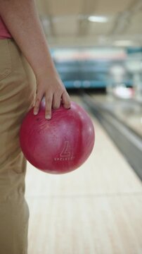 Unrecognizable woman holds 7 weight pink bowling ball before throwing it, vertical video. Player prepares for game in bowling alley, close-up. Technique of holding ball with fingers in bowling.