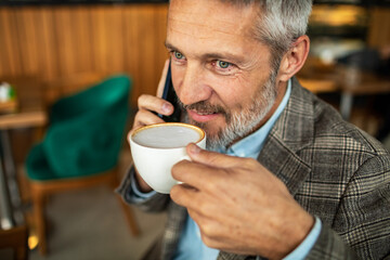 Mature man having coffee while talking on the phone in a cafe