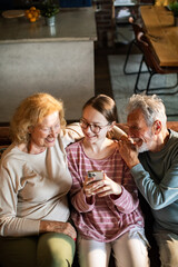 Grandparents and granddaughter using a phone at home